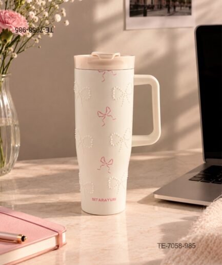 Vaso térmico o jarra con asa lateral y tapa a presión con boquilla, diseño de lazos rosados y lazos formados por perlas o cuentas sobre fondo beige TE7058